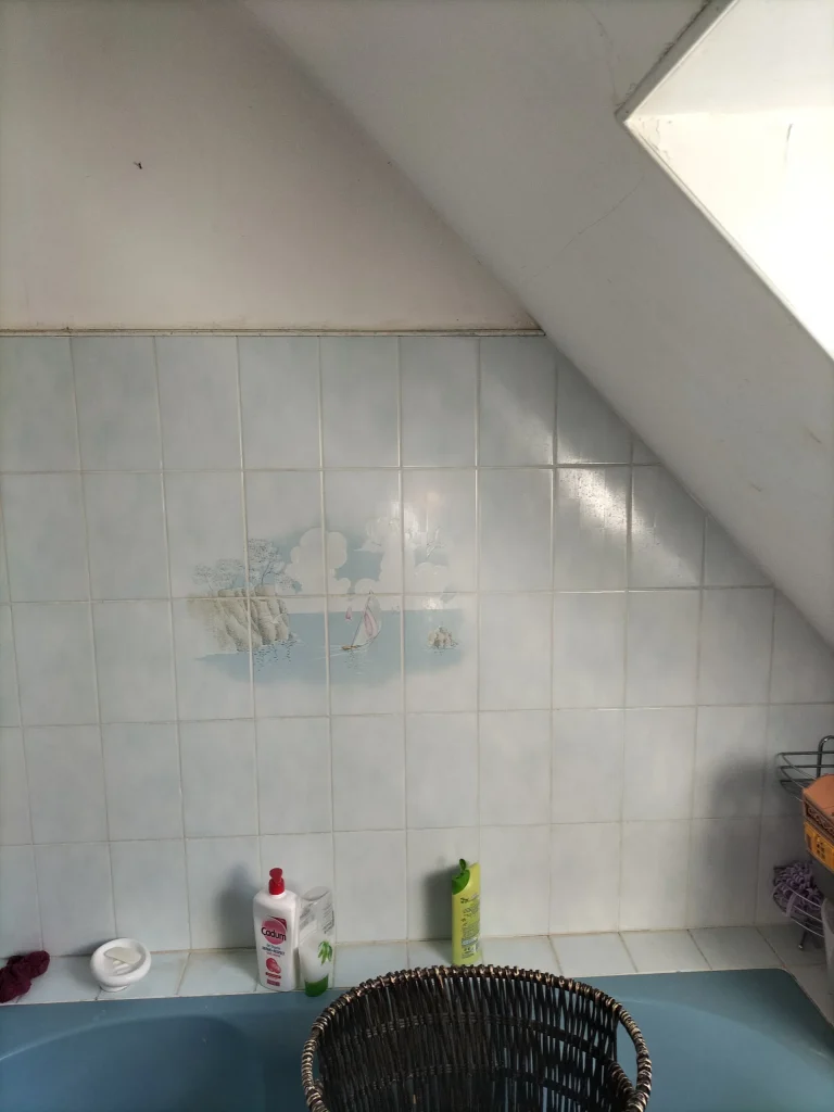 Ancienne salle de bain mansardée avec carrelage mural et baignoire bleue