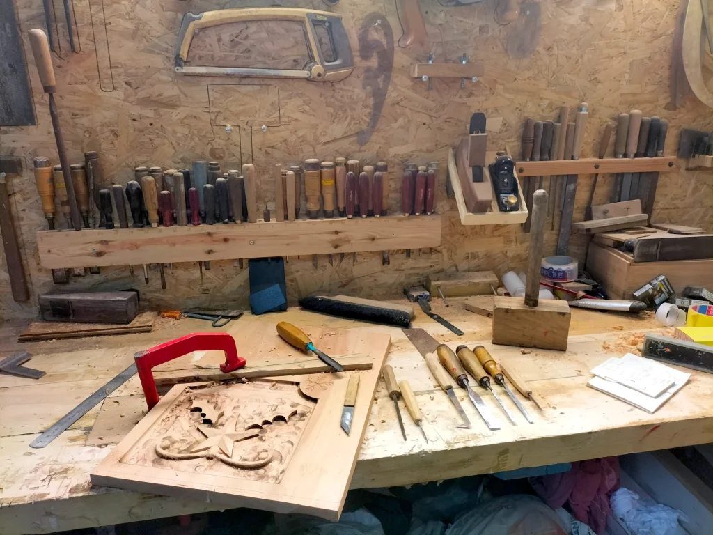 Plan de travail d’un atelier de menuiserie avec outils à bois traditionnels et sculpture en cours de réalisation.