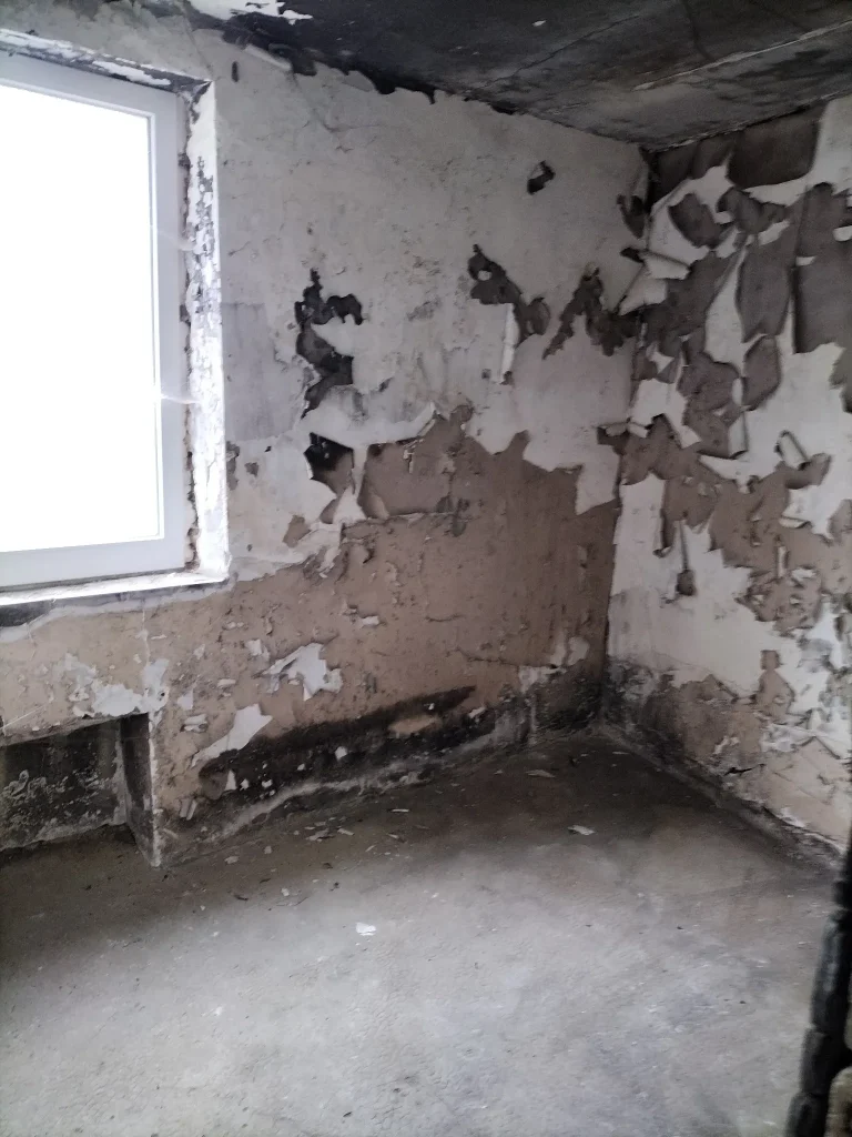 Mur intérieur avec anciens enduits recouverts de peinture écaillée, dégradée par les flammes.