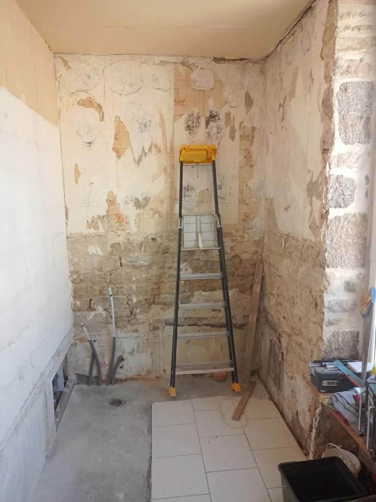 Salle de bain avant rénovation dans l’Orne, murs dégradés et sol partiel.